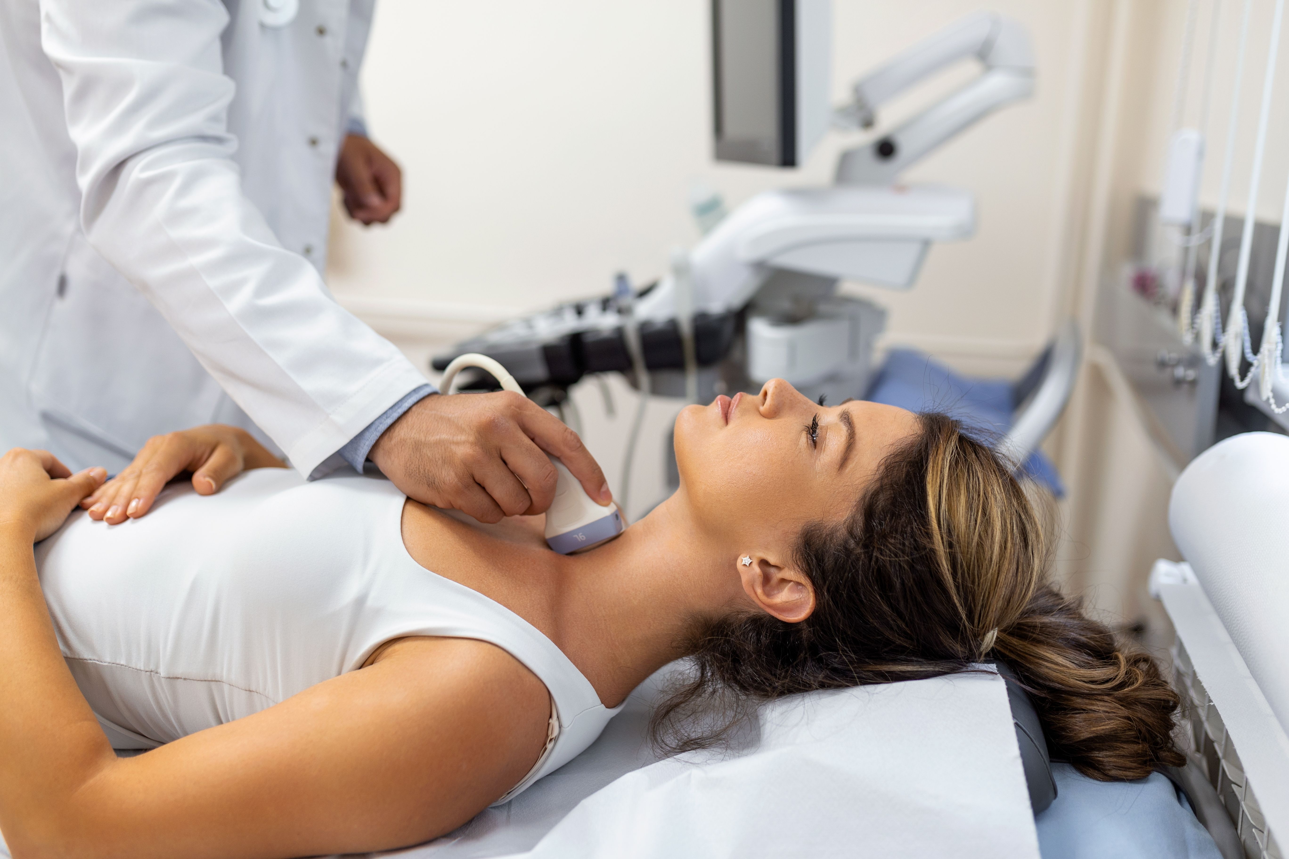 Doctor performs ultrasound scan on woman's neck.
