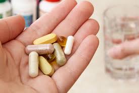 Hand holding various pills near a glass.