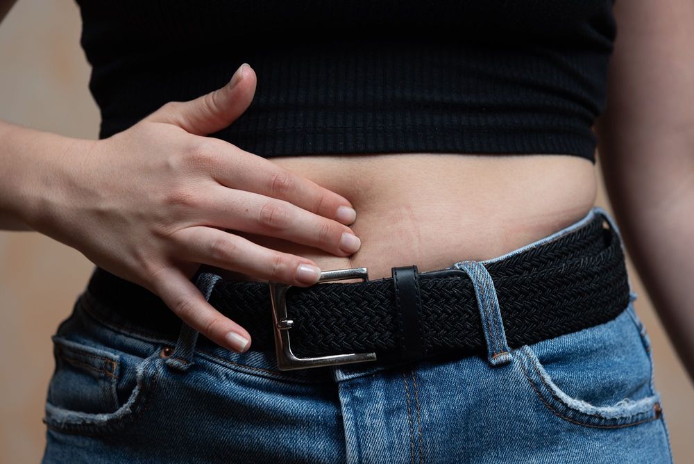 Hand touching a stomach, wearing jeans and black belt.